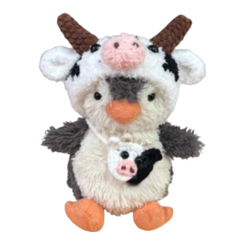 Jellycat Peanut Penguin Bag Charm wearing a dairy cow-themed head cover and holding a matching small bag.