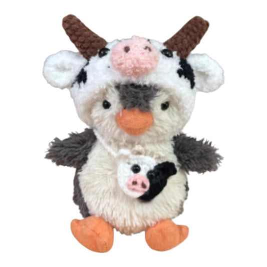 Jellycat Peanut Penguin Bag Charm wearing a dairy cow-themed head cover and holding a matching small bag.